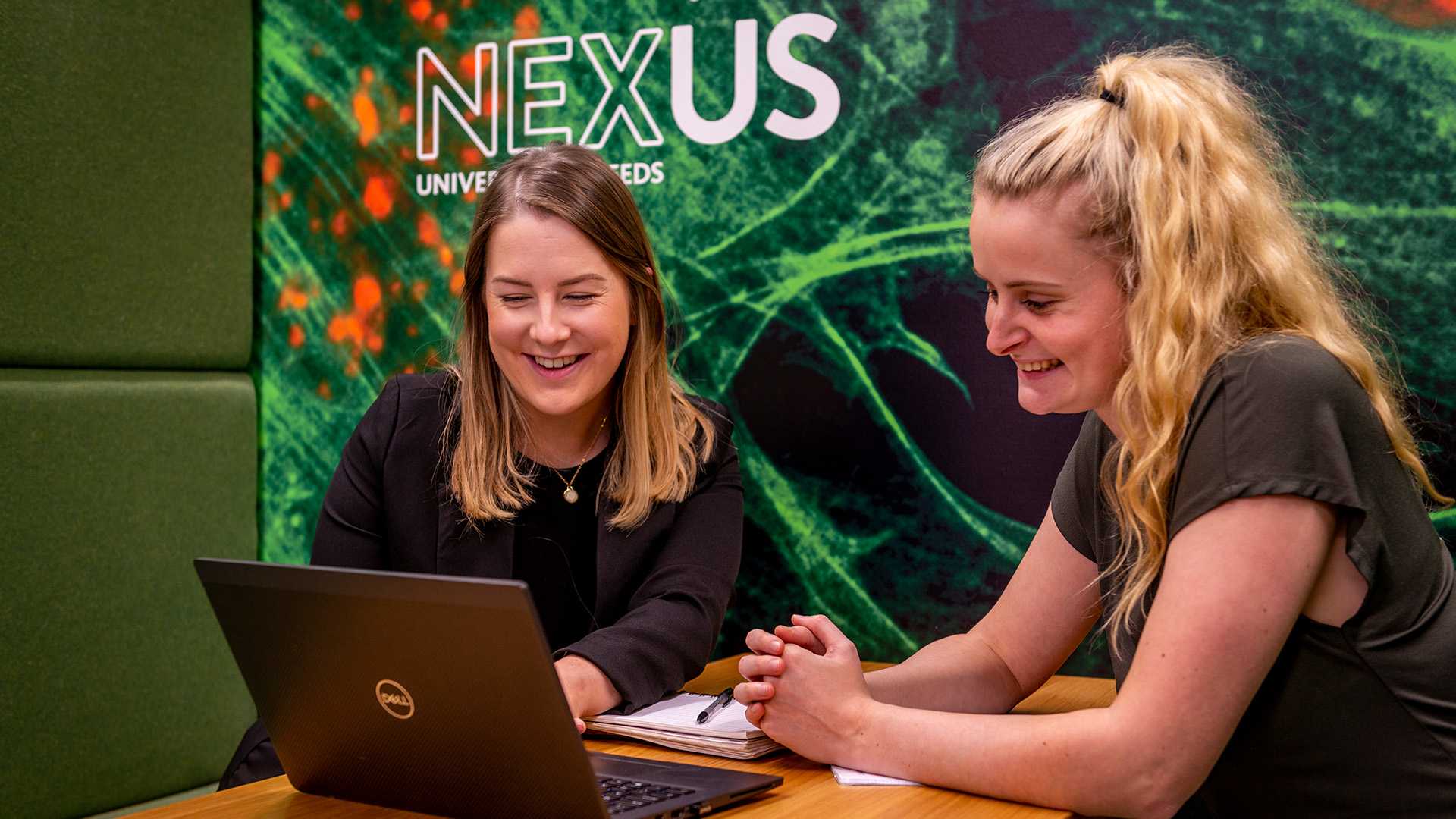 Two people smiling whilst looking at a laptop.